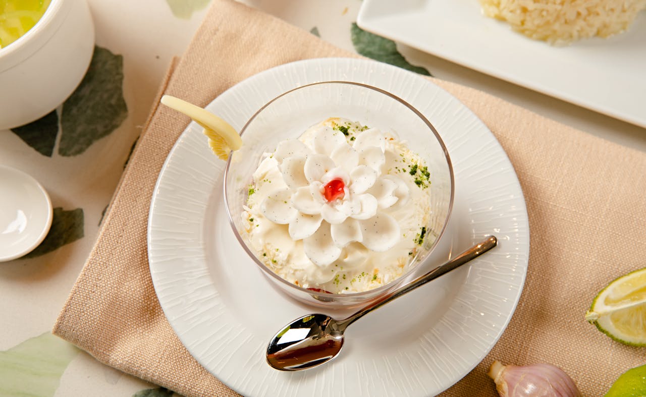 A close-up of a delicious dessert topped with whipped cream and cherry, served elegantly with a spoon.